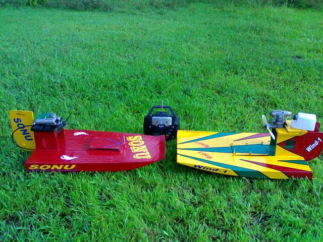 Two nitro methane-powered RC airboats, Sonu and Wind-1, displayed on green grass with a remote controller.